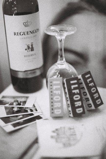 A close-up photograph of a wine bottle labeled 'Requengo' positioned behind an overturned wine glass on a table surface. In front of the glass, there are several printed photographs and several small